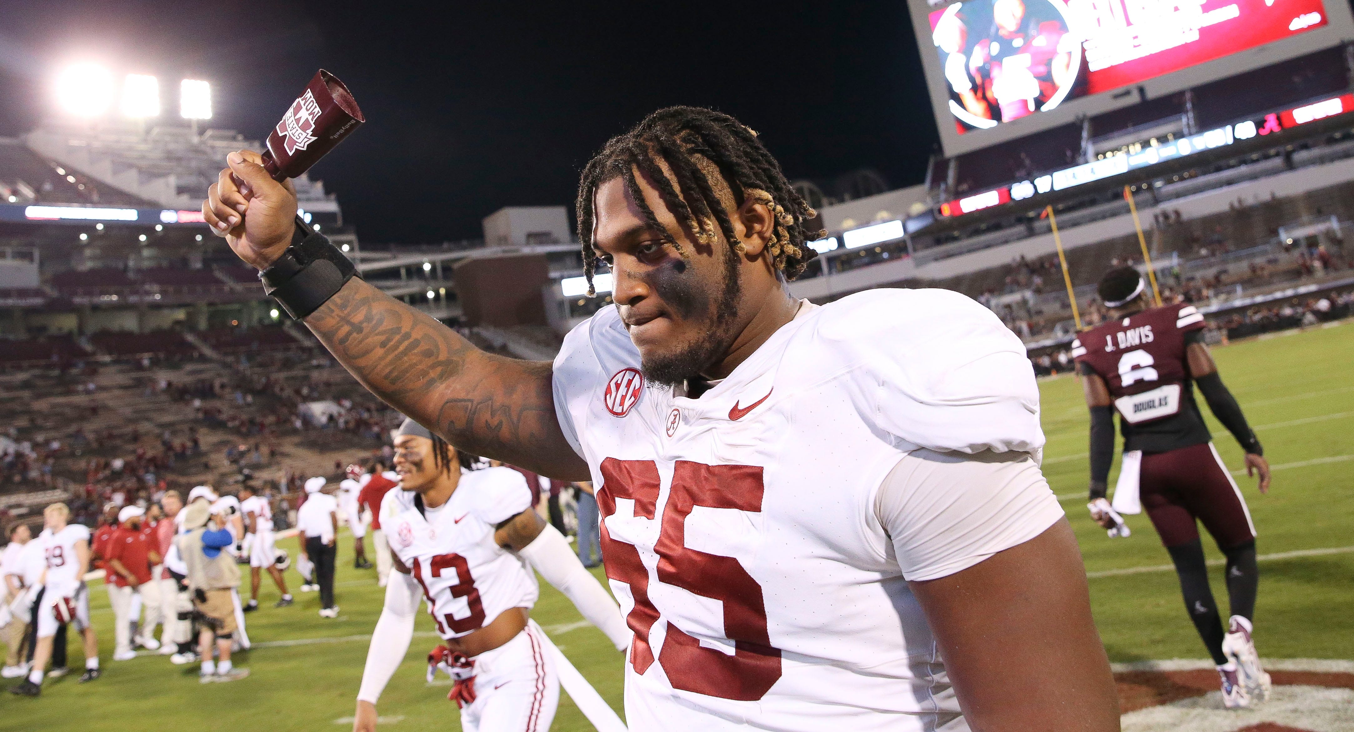 JC Latham holds a cowbell with one hand as he walks off the field